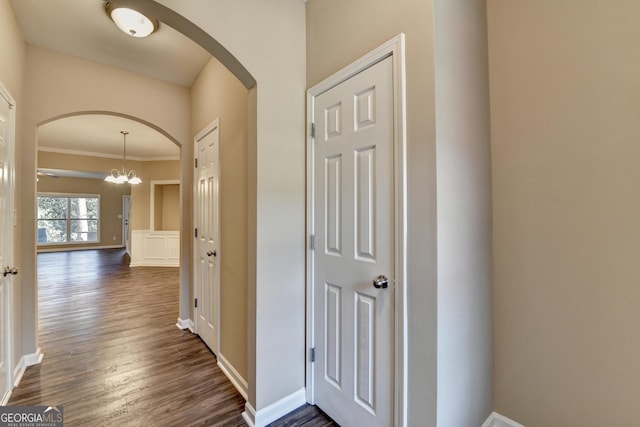 hall featuring dark wood-style flooring, crown molding, baseboards, arched walkways, and a notable chandelier
