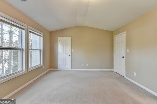 empty room with light carpet, baseboards, and vaulted ceiling
