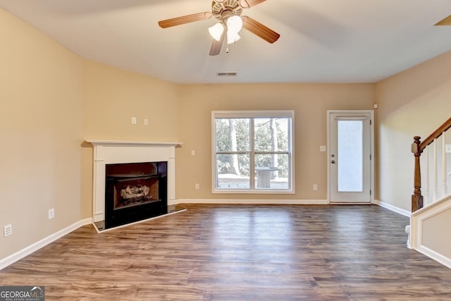 unfurnished living room with stairway, wood finished floors, a fireplace with raised hearth, visible vents, and ceiling fan