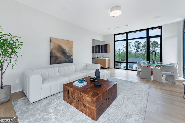 living room featuring a wall of windows, baseboards, and light wood-style flooring