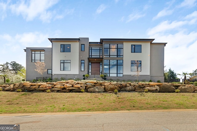 contemporary house featuring stucco siding, a front lawn, and a balcony