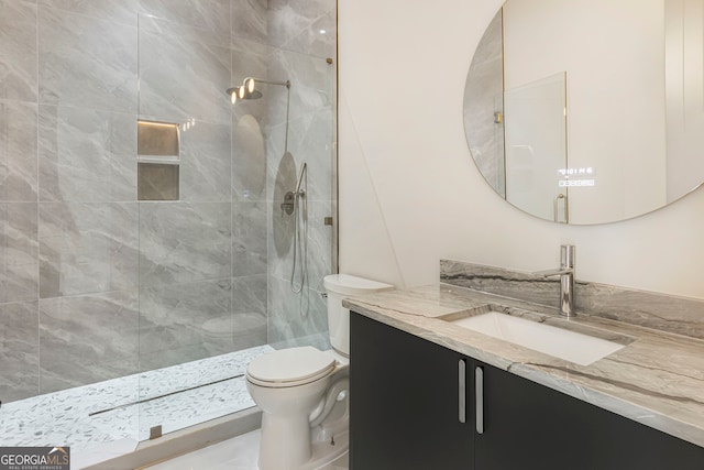 bathroom with a tile shower, toilet, and vanity