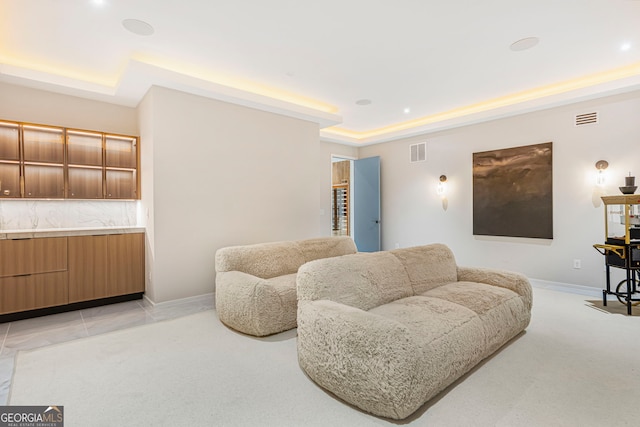 living room with a tray ceiling, visible vents, baseboards, and light carpet