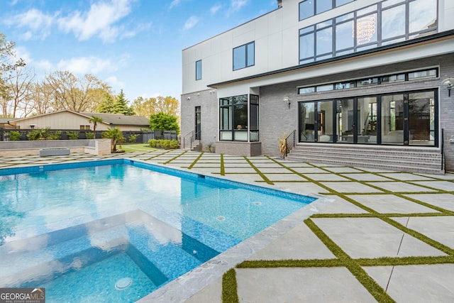 rear view of property with brick siding, fence, a patio area, and a pool with connected hot tub