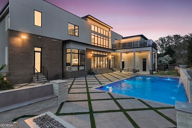 back of property featuring entry steps, a patio area, a balcony, and an outdoor pool