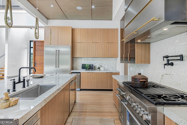 kitchen featuring wall chimney exhaust hood, a sink, high end appliances, modern cabinets, and light stone countertops