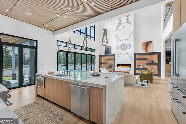 kitchen featuring a sink, modern cabinets, a towering ceiling, appliances with stainless steel finishes, and light stone countertops