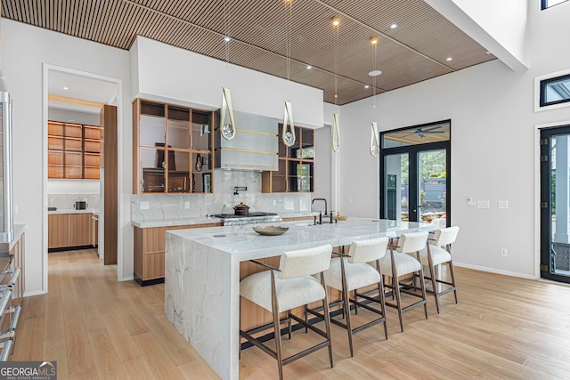 kitchen featuring tasteful backsplash, a large island, light wood-style flooring, wall chimney exhaust hood, and light stone countertops