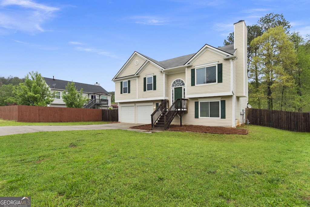split foyer home with concrete driveway, a chimney, a front yard, a garage, and fence