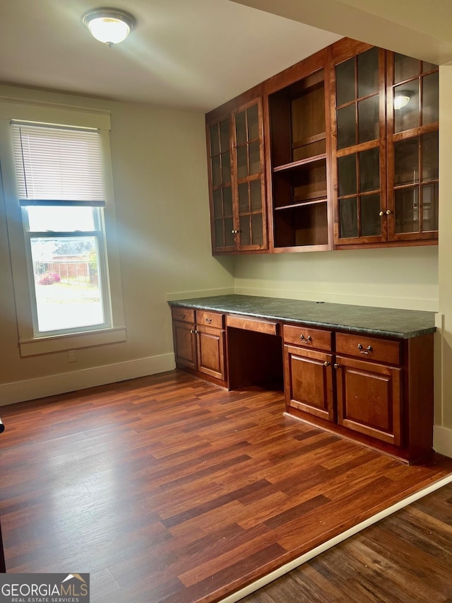unfurnished office with built in desk, baseboards, and dark wood finished floors