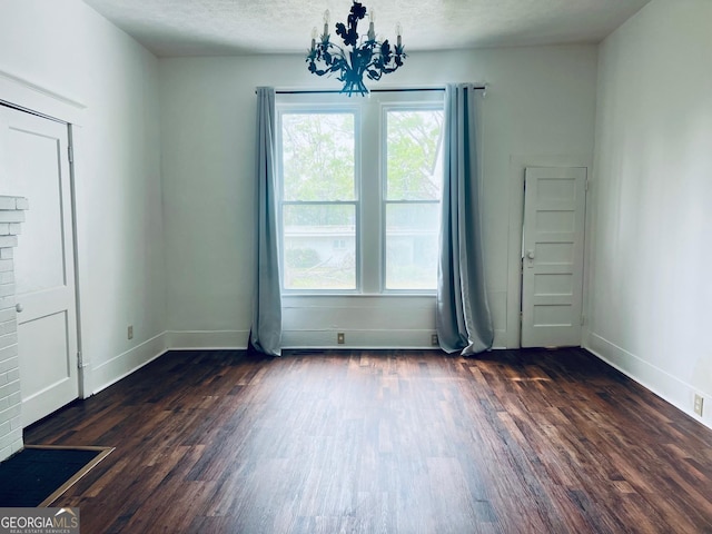 unfurnished room with dark wood finished floors, a wealth of natural light, a notable chandelier, and baseboards
