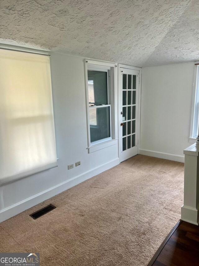 carpeted empty room with baseboards, a textured ceiling, and visible vents
