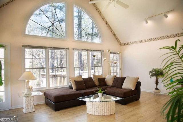 living room featuring track lighting, light wood-style flooring, baseboards, a ceiling fan, and a high ceiling