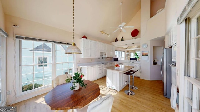 kitchen with freestanding refrigerator, light countertops, ceiling fan, white cabinetry, and a kitchen breakfast bar