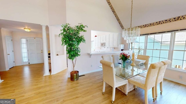 dining room featuring light wood-style flooring, baseboards, an inviting chandelier, ornate columns, and high vaulted ceiling