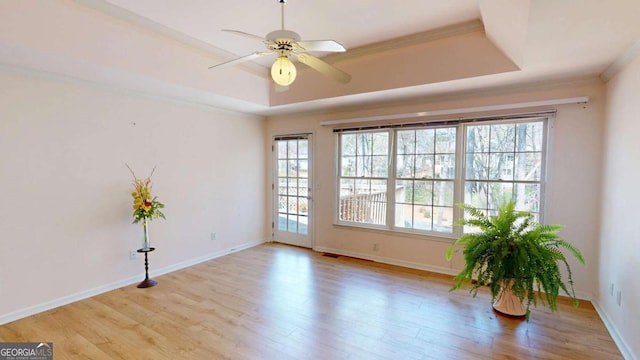 empty room with a ceiling fan, a raised ceiling, a wealth of natural light, and wood finished floors