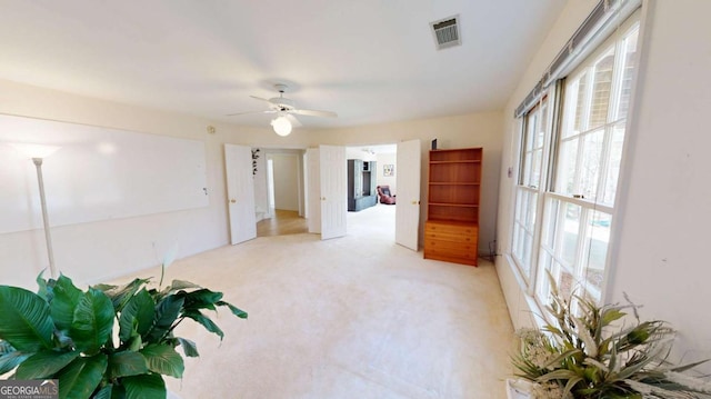 empty room featuring visible vents, a ceiling fan, and light colored carpet
