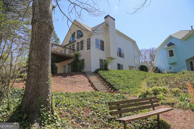 rear view of property featuring a chimney, stairway, and a wooden deck