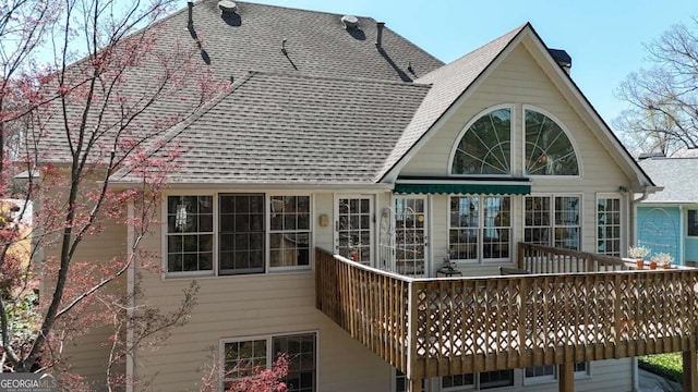 rear view of property with roof with shingles, a deck, and a chimney