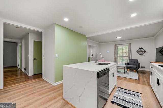 kitchen with white cabinets, light wood finished floors, black dishwasher, a center island with sink, and a sink