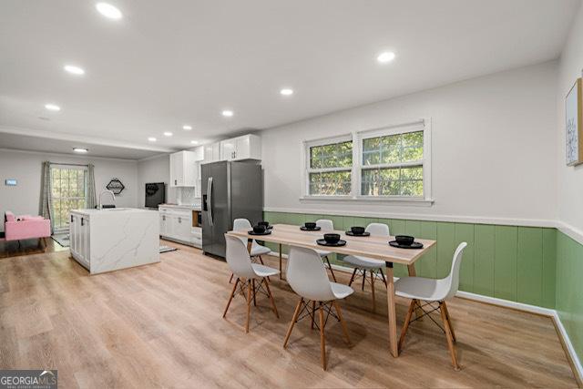 dining room with a wainscoted wall, light wood finished floors, and a healthy amount of sunlight