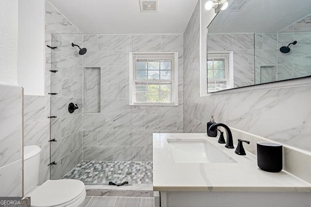 full bath featuring toilet, tiled shower, tile walls, and visible vents