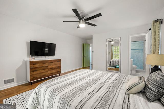 bedroom featuring a ceiling fan, wood finished floors, ensuite bathroom, baseboards, and visible vents