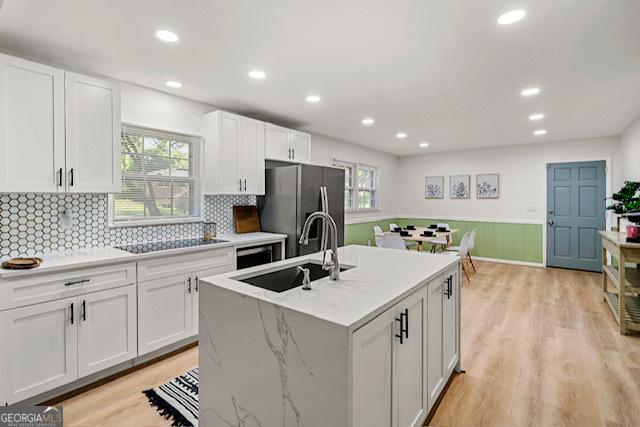 kitchen with a sink, freestanding refrigerator, black electric stovetop, white cabinets, and light wood-style floors