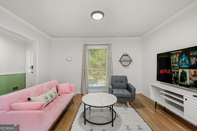 living room featuring baseboards, crown molding, and wood finished floors