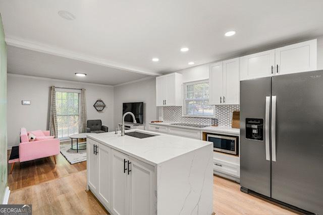 kitchen with tasteful backsplash, appliances with stainless steel finishes, white cabinetry, a sink, and light wood-style floors