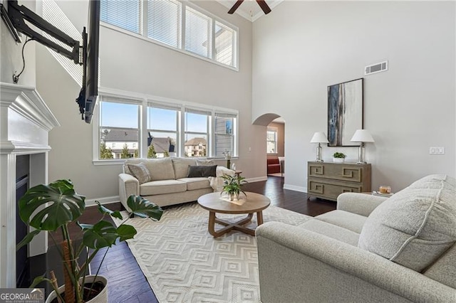 living area featuring arched walkways, a towering ceiling, visible vents, wood finished floors, and ceiling fan