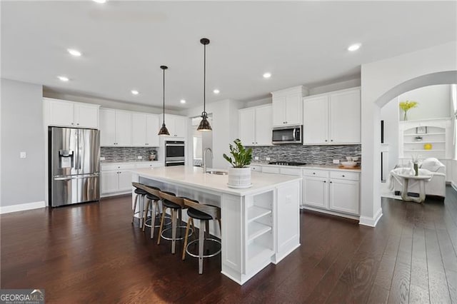 kitchen featuring white cabinets, dark wood-style floors, arched walkways, decorative backsplash, and appliances with stainless steel finishes