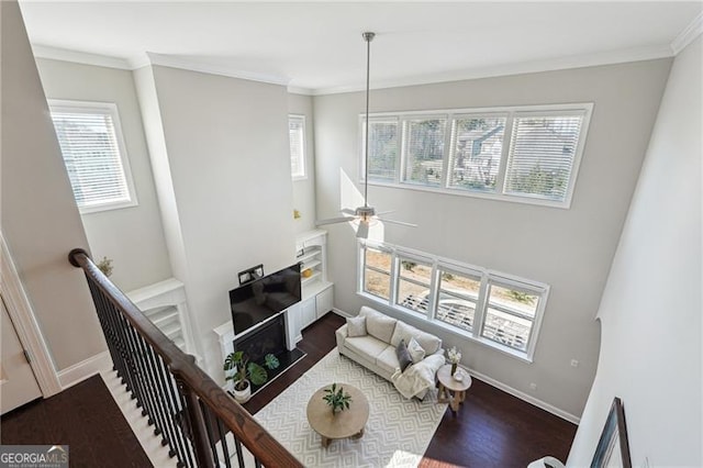 living area featuring baseboards, dark wood-type flooring, ceiling fan, and crown molding
