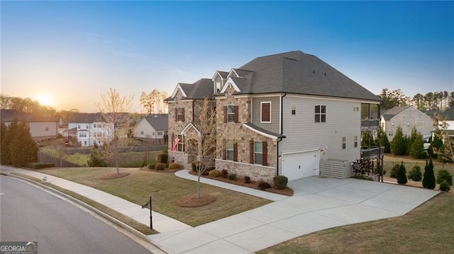 view of front of property with concrete driveway, stone siding, an attached garage, a yard, and a residential view