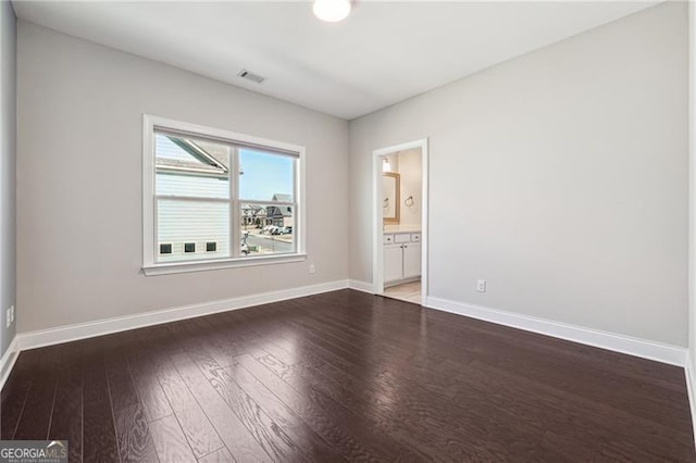 spare room featuring wood finished floors, visible vents, and baseboards