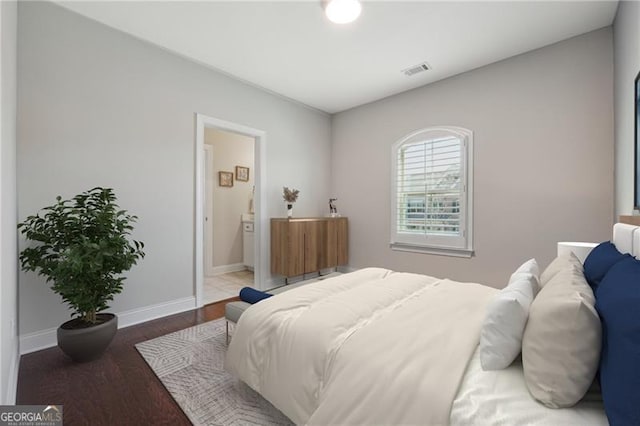 bedroom with baseboards, wood finished floors, visible vents, and ensuite bathroom