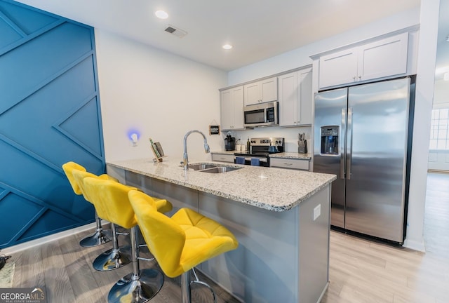 3132 Meadowstone Ln SW, Atlanta, GA 30331 - kitchen featuring appliances with stainless steel finishes, light stone counters, light wood finished floors, a kitchen breakfast bar, and recessed lighting