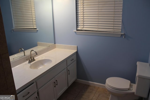 half bathroom with toilet, vanity, baseboards, and tile patterned flooring