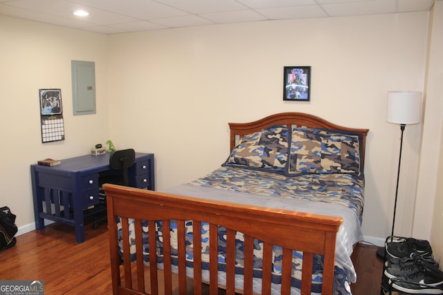 bedroom featuring electric panel, baseboards, wood finished floors, and a paneled ceiling