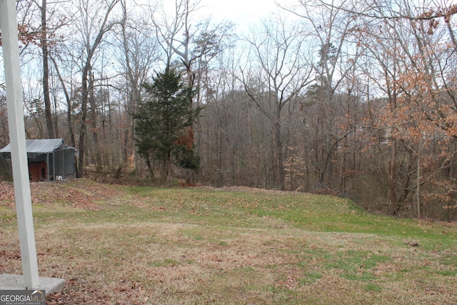 view of yard featuring an outdoor structure, a forest view, and a storage shed