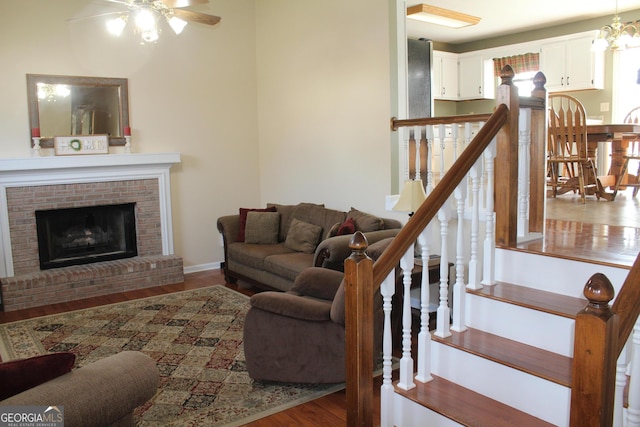 living room with baseboards, ceiling fan, wood finished floors, and a brick fireplace