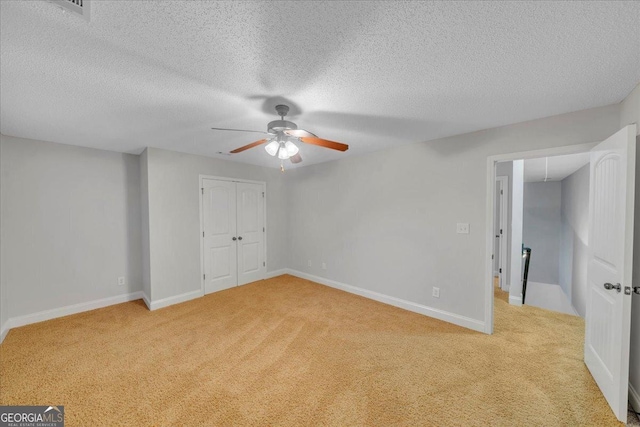 unfurnished bedroom featuring a closet, a ceiling fan, light carpet, a textured ceiling, and baseboards