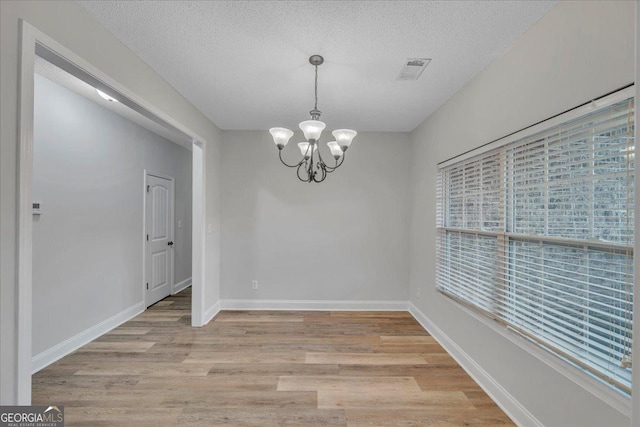 unfurnished dining area with light wood-style flooring, a notable chandelier, baseboards, and visible vents