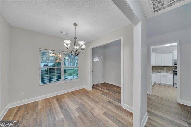 unfurnished dining area with light wood-style flooring, visible vents, and a notable chandelier