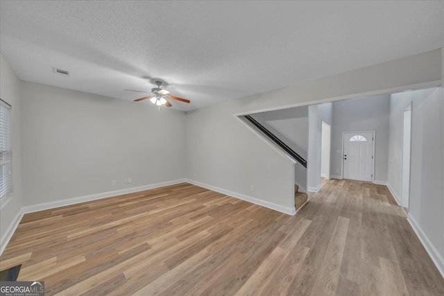 unfurnished room with a textured ceiling, visible vents, light wood-style flooring, stairs, and ceiling fan