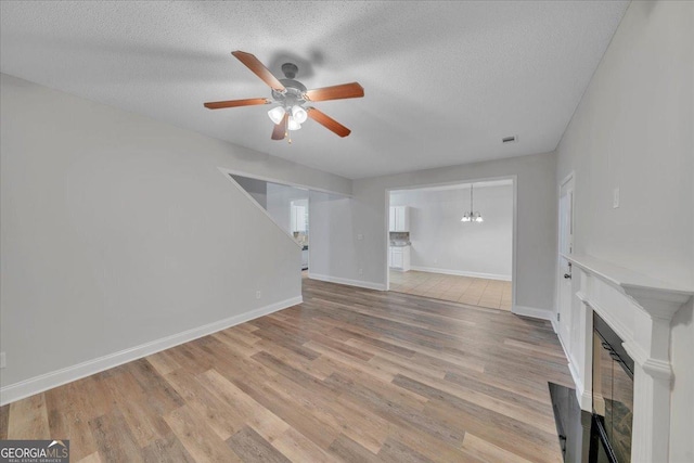 unfurnished living room featuring a textured ceiling, a fireplace, light wood-style flooring, and ceiling fan with notable chandelier