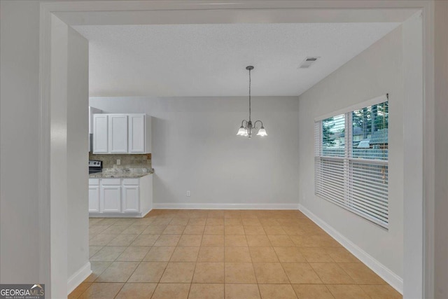 unfurnished dining area featuring a chandelier, a textured ceiling, light tile patterned floors, baseboards, and visible vents