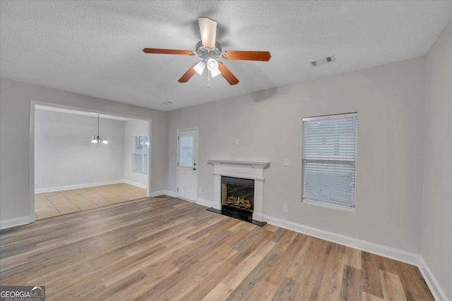 unfurnished living room featuring a ceiling fan, wood finished floors, a fireplace with raised hearth, and visible vents