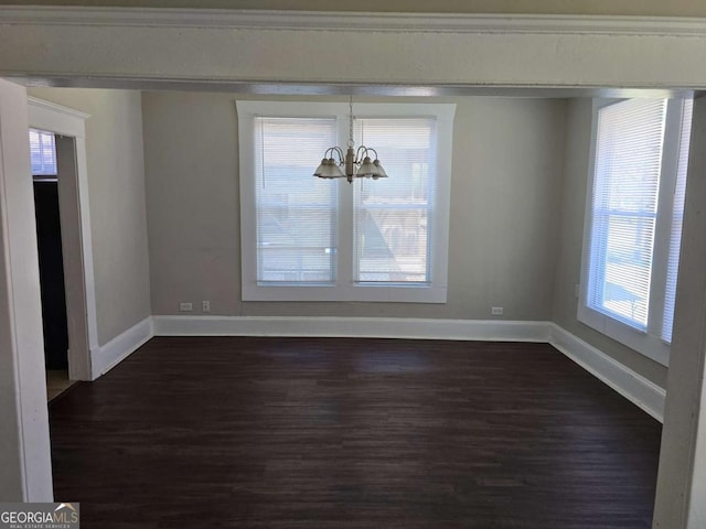 unfurnished dining area with dark wood-style flooring, a notable chandelier, and baseboards