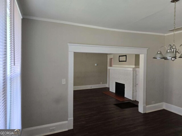 unfurnished living room with a chandelier, wood finished floors, a brick fireplace, baseboards, and ornamental molding